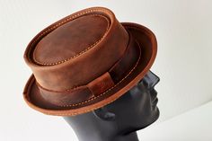 Introducing our handmade, genuine leather hat in a beautiful shade of brown.  The Classic Pork Pie style gives this hat a timeless, elegant look.  Crafted from high-quality leather, this hat is not only stylish but also durable and long-lasting.  Each hat is made by hand, ensuring that every piece is unique and of the highest quality. Perfect for both casual and formal occasions, this hat is a versatile addition to any wardrobe.  Its classic design is sure to never go out of style and it's a mus Classic Brown Hat With Waxed Finish, Rustic Adjustable Brown Top Hat, Classic Brown Hat With Leather Sweatband, Classic Distressed Brown Hat With Short Brim, Fitted Leather Hat With Short Brim, Leather Flat Brim Hat With Leather Lining, Brown Flat Brim Hat With Leather Lining, Adjustable Leather Top Hat With Curved Brim, Brown Hat With Curved Brim And Leather Sweatband