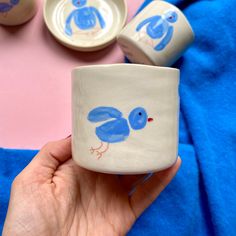 a hand holding a coffee mug with two blue birds painted on the inside and outside