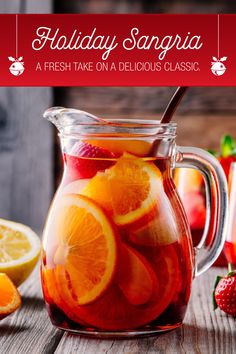 a glass pitcher filled with fruit on top of a wooden table next to sliced lemons and strawberries