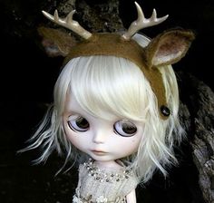 a doll with blonde hair and deer antlers on it's head is standing next to a tree