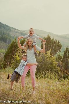 a woman and two children playing in the grass with mountains in the background at sunset