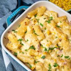 a white casserole dish filled with pasta and corn on the table next to it