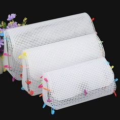 three pieces of white mesh with colorful pins attached to the sides and flowers on each side