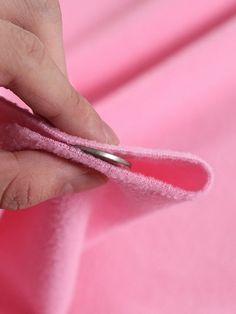 a person is sewing on pink fabric with scissors in their left hand and the other hand holding a pair of scissors