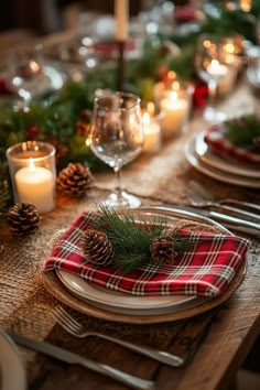 a table set for christmas dinner with pine cones, candles and plaid napkins on it