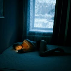 a woman laying on top of a bed in a dark room next to a window