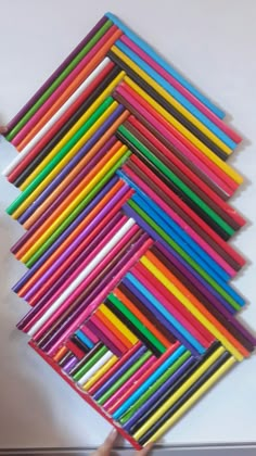 a stack of colored pencils sitting on top of a white table next to a person's hand