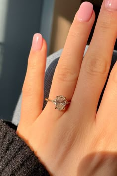 a close up of a person's hand with a pink manicure and an engagement ring