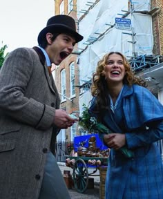 a man and woman standing next to each other in front of a building with scaffolding