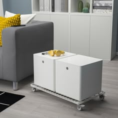 a living room with a gray couch and white storage containers on wheels in front of it