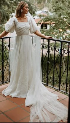 a woman in a white dress standing on a balcony with her hands on the railing