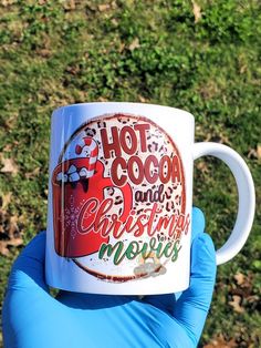 a person in blue gloves holding up a coffee mug with the words hot cocoa and christmas movies on it