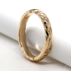 a gold wedding band with flowers and leaves on the side, sitting on top of a white