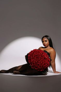 a woman sitting on the ground holding a large red rose