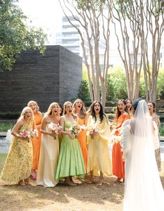 a group of women standing next to each other in front of trees and bushes with flowers