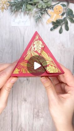 someone is holding up a red and gold origami triangle with an arrow in the middle