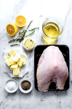 raw chicken and ingredients laid out on a white marble counter top, including lemons, garlic, parmesan cheese, butter, and seasoning