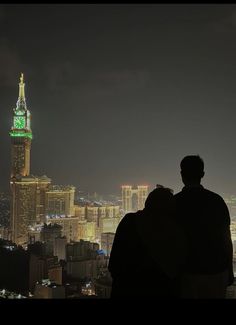 two people are looking out at the city lights and skyscrapers in the night time