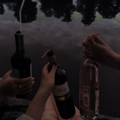 two people are holding wine bottles near the water while another person holds something in their hand