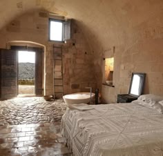 a bedroom with stone walls and flooring has a large bed in the middle, an open doorway leading to another room