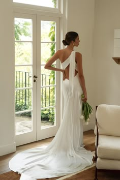 a woman standing in front of a door wearing a white dress and holding a bouquet