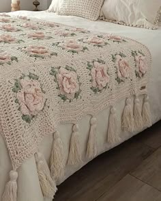 a crocheted bedspread with pink flowers and tassels