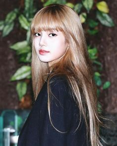 a woman with long blonde hair standing in front of a plant