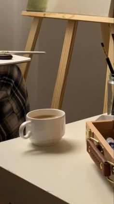 a cup of coffee sitting on top of a table next to a painting easel