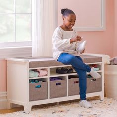 a woman sitting on top of a white bench in a room with pink walls and drawers