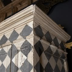 an old cabinet with black and white checkered paint on the top, next to a clock