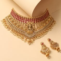 Description A cascading choker fit for a bride, this intricate choker neckpiece is the definition of regalia and opulence, studded with fine CZ and semi-precious Kempu stones. A head-turner, this gold plated nakshi temple choker features a parade of elephants centered with Goddess Lakshmi motif. Gold drop beads add royal charm to this necklace. Details & Specifications: Materials used: Brass Alloy with Antique Gold Plating Weight – Choker 135.62 gm, Earrings 24.16 gm Length – Choker 19 cm, Earri Luxury Temple Jewelry Choker For Women, Luxury Temple Jewelry Choker For Ceremonial Occasions, Chokers Gold Indian Bridal Jewelry, Festive Temple Jewelry Bridal Choker Necklace, Festive Temple Jewelry Bridal Choker, Wedding Temple Jewelry Choker Necklace, Heavy Temple Jewelry Bridal Choker Necklace, Heavy Temple Jewelry Style Bridal Choker Necklace, Heavy Temple Jewelry Style Bridal Choker