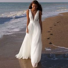 a woman in a white dress walking on the beach