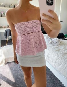 a woman taking a selfie with her cell phone in the mirror while wearing a pink crocheted top