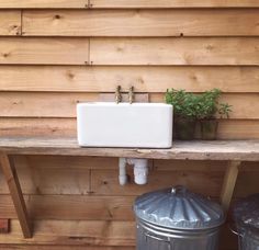 a white sink sitting on top of a wooden shelf next to a trash can and potted plant