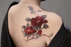 a woman's back tattoo with red flowers and leaves on her left shoulder,