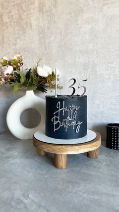 a black and white birthday cake sitting on top of a wooden stand next to a vase with flowers