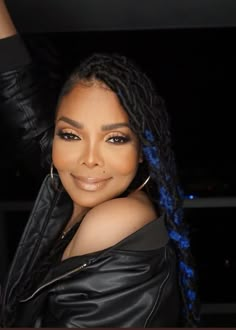 a woman with long braids in a black leather jacket posing for the camera at night