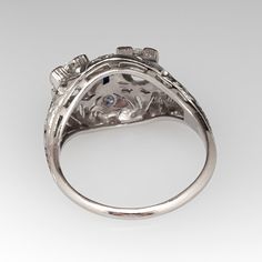 This Toi et Moi, circa 1920s, diamond ring features a pierced design with engraved details and is accented with two (2) old European cut diamonds set into four-prong settings, four (4), bead set, round single cut diamonds and one (1), bezel set, rectangular French cut synthetic blue sapphire. The ring measures 12.5mm at the top, rises 7.5mm above the finger, tapering to 1.7mm wide and 1.2mm thick at the base of the shank. It is currently a size 8. Antique Three Stone Round Diamond Ring, Antique Oval Three Stone Diamond Ring, Antique Three Stone Round Cut Rings, Art Deco Brilliant Cut Diamond Ring Collectible, Art Deco Collectible Diamond Ring With Brilliant Cut, Antique Three Stone Round Rings, Antique Platinum Three Stone Diamond Ring, Antique Three Stone Diamond Ring In Diamond White, Antique Three-stone Diamond Rings