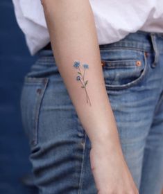 a small blue flower tattoo on the left arm