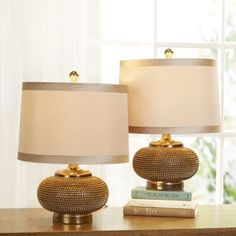 two lamps sitting on top of a wooden table next to a book and lamp shade