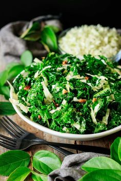 a white bowl filled with greens and rice on top of a wooden table next to green leaves