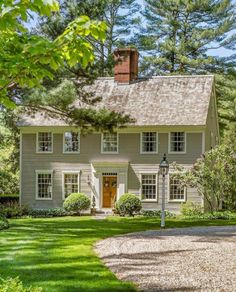 a white house surrounded by lush green trees and bushes in the foreground is a gravel path leading up to it's front door