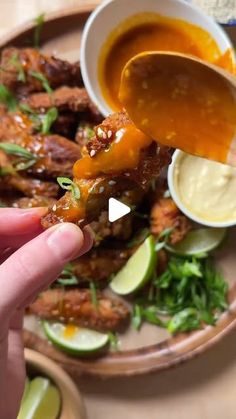 a person dipping sauce on top of chicken wings with limes and cilantro