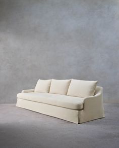 a white couch sitting on top of a floor next to a gray wall with no one in it