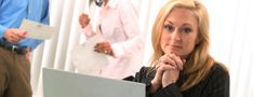 a woman sitting in front of a laptop computer with her hands on her chin looking at the camera