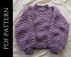 a purple knitted sweater laying on top of a white bed sheet with the words happy pattern written across it