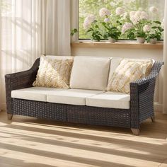 a wicker couch sitting in front of a window with flowers on the windowsill