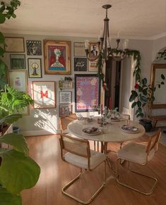 a dining room table with chairs and pictures on the wall behind it, in front of a potted plant