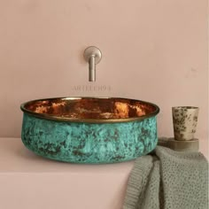 a copper sink with green pattered paint on it and a cup next to it