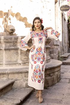 This Beautiful Mexican Floral Dress is the perfect dress for a special event or Mexican Fiesta.  It reflects the Mexican culture through its unique embroidered design and vibrant colors.  It has laces to tie on the back for an adjustable and comfortable fit.  It is embroidered by Artisanal Machine- hand manipulated by Mexican Artisans in Guanajuato, Mexico. It's made out of fresh Mexican Cotton and is full of embroidered multicolor flowers. Size S - XL Shop more Mexican Dresses here:  https://ww Traditional Dresses Mexican, Mexican Clothes Women, Mexican Style Outfits, Mexican Wedding Dress Embroidered, Mexican Dresses For Women, Mexican Wear, White Mexican Dress, Mexican Outfit Ideas, Mexican Theme Dresses